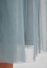 Tessuto di tulle azzurro chiaro con una texture trasparente, caratterizzato da sezioni sovrapposte e un orlo leggermente irregolare, creando drappeggi delicati e fluenti.