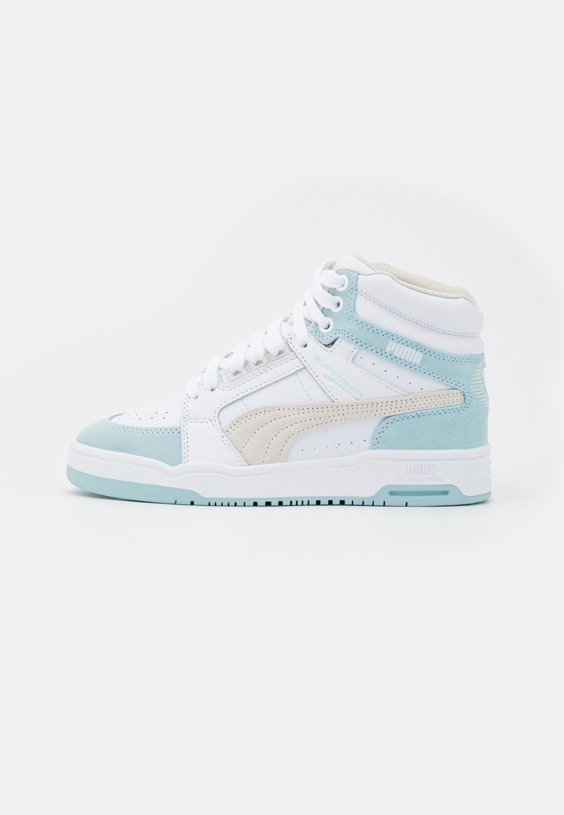 Baskets montantes blanches et bleu clair avec une bande latérale beige, bout perforé et lacets blancs sur fond blanc.