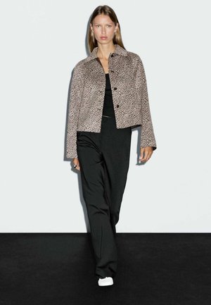 Veste courte en imprimé léopard en tissu doux, dotée d'un col et de boutons noirs, associée à un pantalon large noir et des baskets blanches.