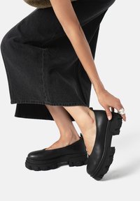 Zapatos de plataforma de cuero negro con suela de goma gruesa. Presentan una punta redondeada y un diseño minimalista. Textura suave con construcción duradera.