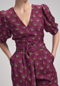 Vestido de manga corta en burdeos con un estampado de palmeras en verde y rosa, con un escote en V profundo y una cintura ceñida con un cinturón y una hebilla circular.