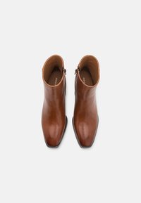 Bottines en cuir marron avec un bout pointu, texture lisse, fermeture éclair sur le côté et design minimaliste. L'intérieur présente l'étiquette de la marque.