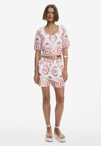 Vit kort topp och matchande shorts med livfulla röda, orange och lila cirkulära mönster. Mjuk tyg, avslappnad passform och snörningsdetalj.