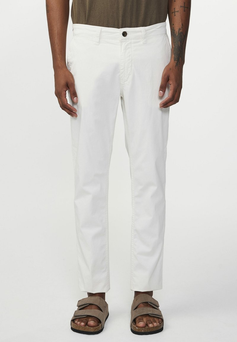 Białe, lekkie spodnie o prostym kroju, z zapięciem na guzik i bocznymi kieszeniami, zestawione z brązowymi sandałami na płaskim obcasie.