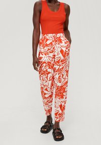 Röd ribbad tanktop i kombination med vita byxor med ett djärvt rödblommigt mönster, elastisk midja och sidofickor. Bärs med svarta sandaler.