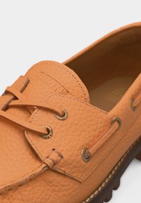 Mocassins en cuir couleur tan avec laçage frontal, œillets en métal et détail de coutures texturées.