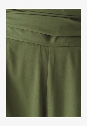 Tela verde oliva con textura suave, con una pretina doblada y costuras verticales que le dan una apariencia estructurada.