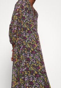 Robe fleurie sur fond noir, avec des fleurs vibrantes de couleur violette, jaune et rose. Manches bouffantes et décolleté en V.