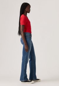 Red ribbed short-sleeve top paired with light blue flared jeans. The outfit features a fitted silhouette and classic black sneakers with white accents.