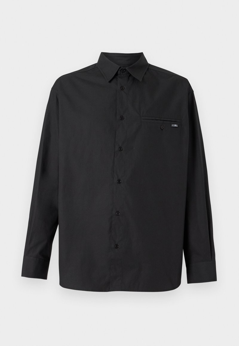 Chemise noire à manches longues en tissu lisse, avec un col, une patte de boutonnage, une poche poitrine unique et un logo discret sur la poche.