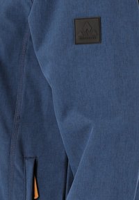 Sininen takki, jossa on sileä, teksturoitu kangas. Varustettu mustalla logo-tarralla ja sivutaskulla. Yksinkertainen, moderni muotoilu puhtailla linjoilla.