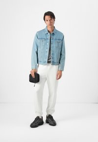 Lichtblauwe denimjack, grijze top, witte joggers, zwarte sneakers, holding een kleine zwarte pouch. Eenvoudig ontwerp, ontspannen pasvorm overal.