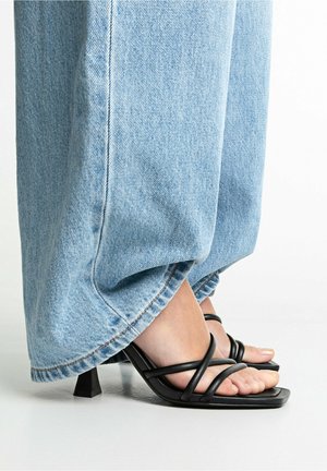 Sandalias negras con tiras, punta cuadrada y tacón bajo cuadrado, combinadas con vaqueros de mezclilla azul claro de corte holgado y dobladillo desflecado.