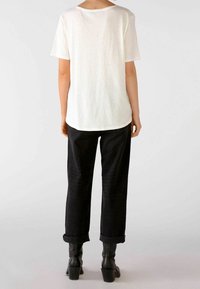Hvid kortærmet t-shirt med en afslappet pasform, der har en rund halsudskæring. Sammen med rullet sorte bukser og ankelstøvler.