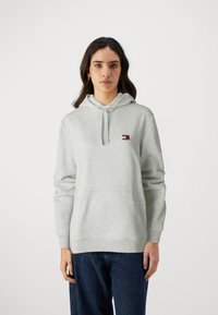 Sudadera con capucha gris hecha de un tejido suave, con un pequeño logo en el pecho, bolsillo tipo canguro y puños y dobladillo acanalados.