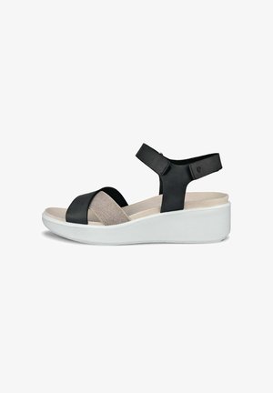 Svart och beige sandal med ett mjukt tygband, justerbart vristband och en vit plattformssula. Minimalistisk design, bekväm passform.