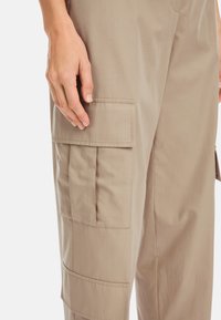 Beige Cargo-Hosen mit mehreren Taschen und einer lockeren Passform. Der Stoff ist glatt und leicht, ideal für den Alltag.