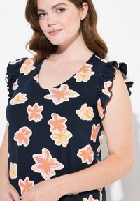 Blusa floreale navy con fiori rosa e crema, scollo a V e maniche volant. Tessuto morbido con una vestibilità comoda.