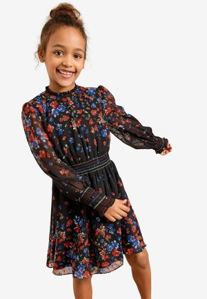 Abito nero floreale con maniche lunghe trasparenti, vita arricciata e fiori multicolori (rossi, blu, verdi) sparsi nel tessuto.
