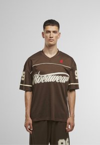 Barna sportmez rövid ujjakkal, fehér írásjellel ellátott "Rocawear" logóval és piros kiegészítéssel, 89-es mezszámmal, amely fehér színben található az ujjakon.