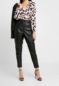 Blusa de estampado de leopardo con mangas largas, combinada con pantalones de cuero negros de cintura alta. La modelo lleva tacones negros con tiras.