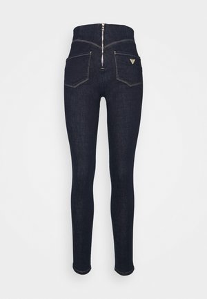 Høj talje mørkeblå skinny jeans med lynlås bagpå, to baglommer med syningsdetaljer og et lille trekantet mærkelogo på højre lomme.