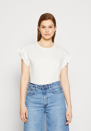 T-shirt bianco a maniche corte con dettagli in pizzo sulla manica, abbinato a jeans in denim blu a vita alta. Tessuto dalla texture liscia.