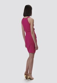 Tailliertes pinkes Kleid aus strukturiertem Stoff, mit ärmellosem Design und passendem Taillenbund, kombiniert mit schmalen goldenen High-Heels.