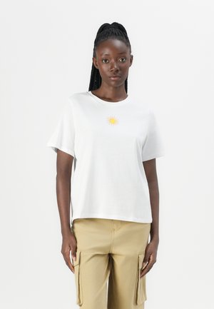 T-shirt bianco in cotone con maniche corte e scollo tondo. Presenta una piccola grafica di un sole giallo sul petto. Vestibilità ampia.