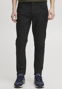 Črne hlače v slim fit kroju, izdelane iz mehkega, elastičnega materiala. Imajo pasne zanke, sprednje žepe in diskretne stranske dodatke.