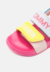 Kleurige sandalen met een roze textuurzool, gele klittenbandsluiting met "TOMMY" branding en een witte band met roze tekst voor extra detail.