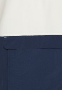 Jupe bleu marine avec une large ceinture et un petit détail de couture turquoise sur fond blanc.