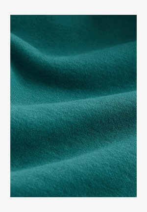 Tkanina s teksturom u dubokoj petrolejsko plavoj boji; mekana i blago dlačasta površina s suptilnim uzorkom tkanja, koja pokazuje bogatu boju i ujednačenu teksturu.