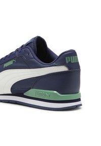Baskets Puma avec une tige en cuir bleu marine, un panneau latéral blanc et des accents verts. Dotées d'un col rembourré et d'une semelle en caoutchouc texturée.