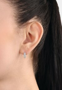 Pendiente de aro de plata que presenta tres filas de pequeñas piedras preciosas transparentes, destacando un acabado suave y pulido, y un diseño cilíndrico compacto.