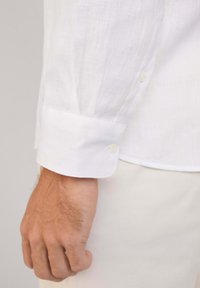 Poignet de chemise en lin blanc avec fermeture à bouton et un subtil détail brodé. La texture lisse et le matériau léger améliorent la respirabilité.
