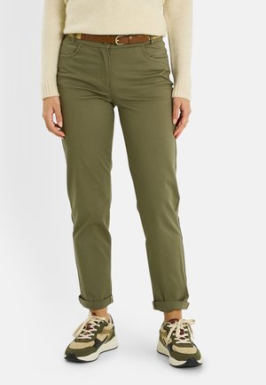 Pantalones entallados verde oliva con bolsillos delanteros y puños doblados, combinados con zapatillas multicolores y un cinturón marrón sobre un suéter claro.