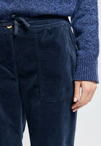 Pantalons en velours côtelé bleu marine avec taille à cordon de serrage, poches avant et texture douce, associés à un pull bleu texturé.