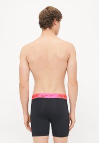 Schwarze Boxershorts für Männer mit einem breiten pinken Nike-Logo-Bund, ausgestattet mit einer glatten Textur und einem taillierten Design. Rückansicht dargestellt.