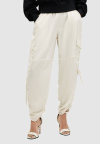 Crème kleur cargo broek met een losse pasvorm, elastische boorden, zijzakken en trekkoorden. Gekleed met witte haksandalen.
