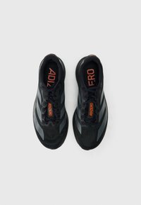 Zapatillas deportivas negras con una parte superior texturizada, que cuentan con detalles reflectantes en gris, cordones negros y la palabra "ADIZERO" en naranja en la lengüeta.