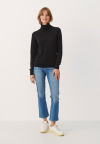 Črn pulover s turtleneck ovratnikom, v kombinaciji z svetlo modrimi ravnimi hlačami in belimi teniskami z rumenim podplatom. Preprost dizajn, mehak material.