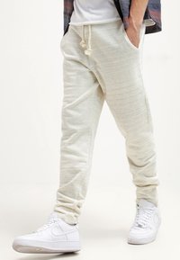 Ljusgrå joggerbyxor gjorda av mjukt, texturerat tyg med elastisk midja och dragsko. Åtföljs av vita sneakers.