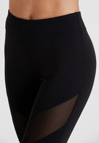 Svarta leggings med hög midja, med mesh-paneldetaljer på sidorna för andningsförmåga och en slimmad, figurnära design.