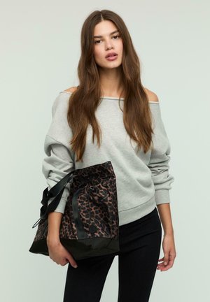 Felpa grigia con design scivolato sulle spalle, abbinata a una borsa strutturata in pelle leopardata nera e marrone con chiusura a coulisse e manici.