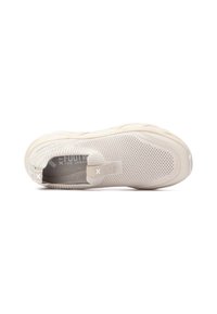 Zapatilla deportiva de color beige claro con parte superior de malla transpirable, suela texturizada y una lengüeta para ponerla fácilmente. Diseño minimalista con una marca sutil.
