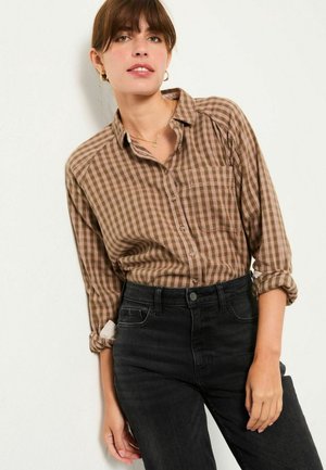 Brown and cream checked button-up shirt with long sleeves, rolled cuffs, and a left chest pocket, paired with high-waisted black jeans.
