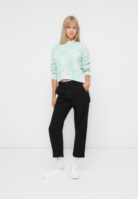 Lyse turkise strikkegenser med kort hem, kombinert med svarte tapered bukser og hvite joggesko. Enkle og teksturerte detaljer.