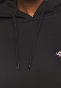 Svart huvtröja i bomull, med en ficka fram, dragsnutar och en liten färgglad logotyp patch på bröstet.