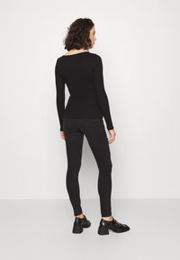 Top negru cu mânecă lungă și un design ajustat, asortat cu blugi skinny negri și botine negre cu toc gros.